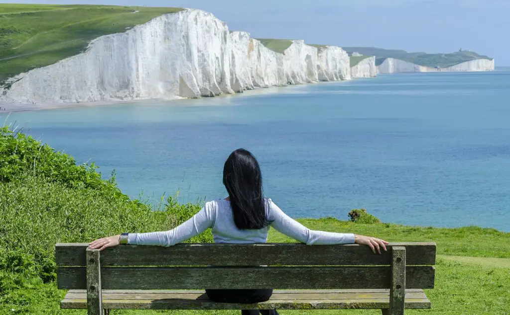 A woman relaxes on a bench, admiring the scenic cliffs and ocean view.